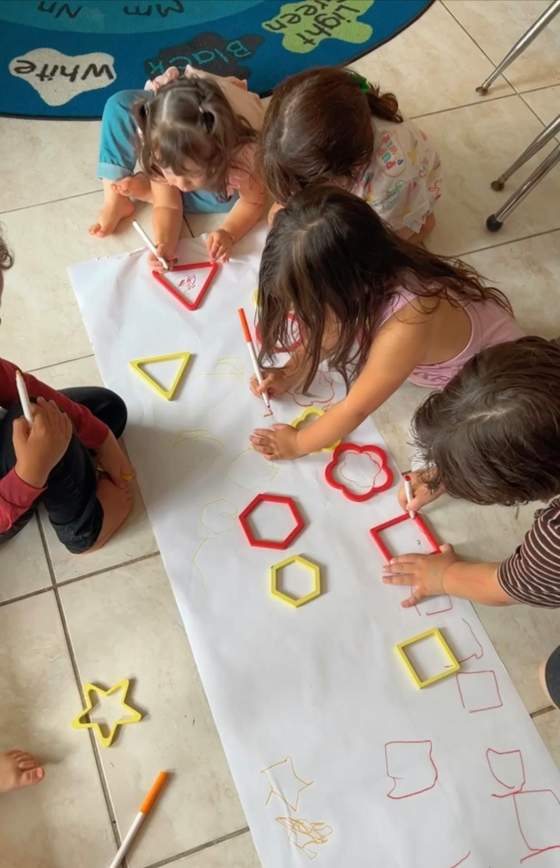 Children tracing shapes on a large sheet of paper on the floor