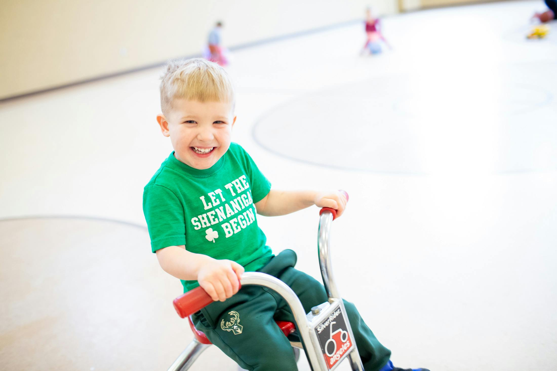 Child in green shirt riding a tricycle indoors