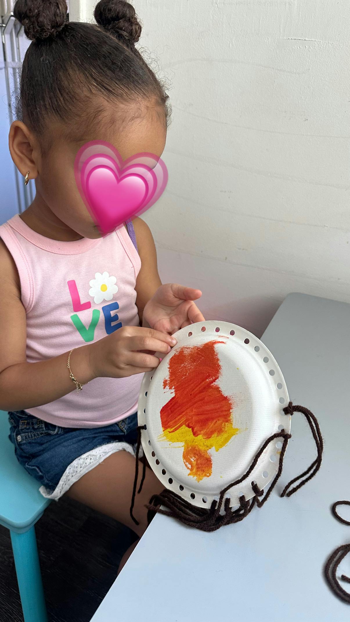 Child threading yarn through a painted paper plate craft