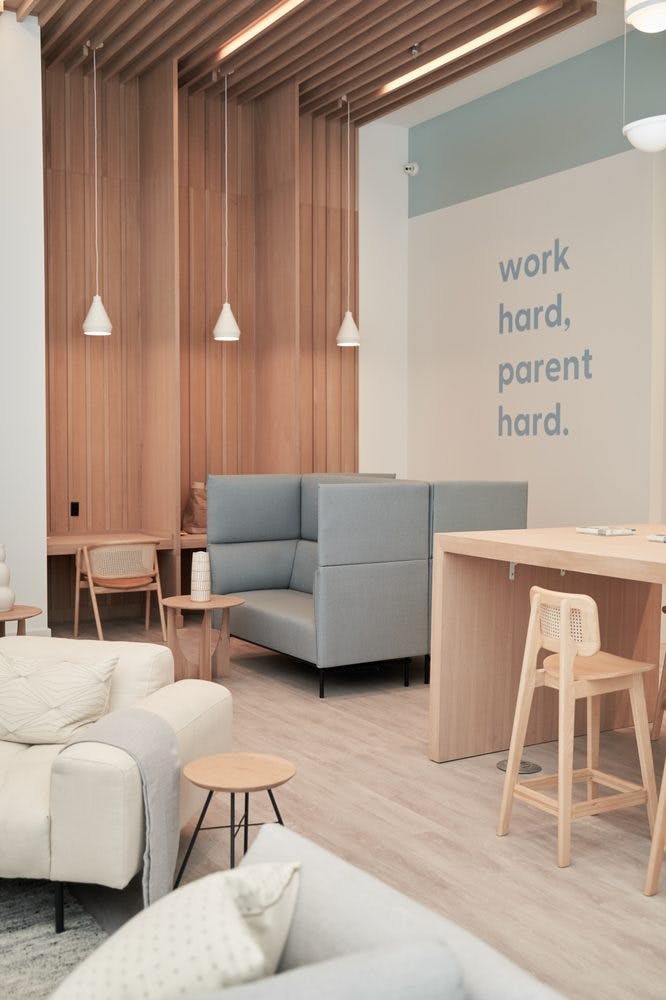 Lounge area with couches, high-backed booths, and a wall with text "work hard. parent hard." text"