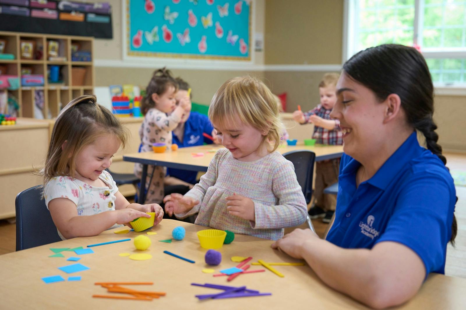 Adult and two children playing with craft supplies at a table in a classroom