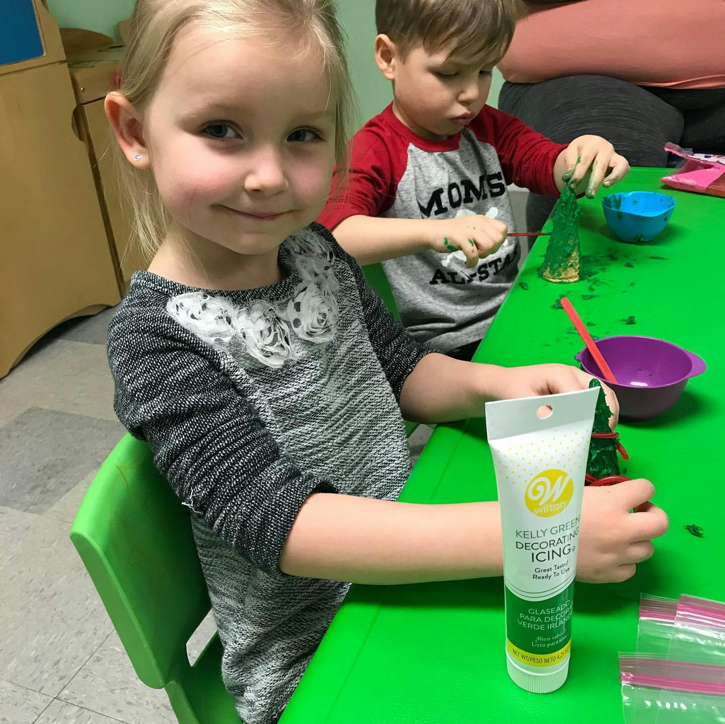 Child holding a tube of icing at a green table with another child