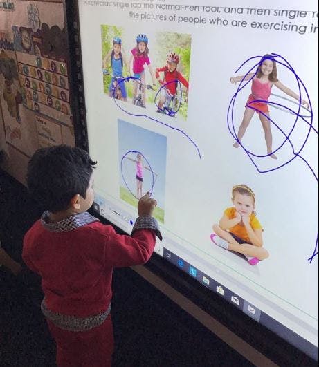 Child interacting with an interactive whiteboard displaying images of children