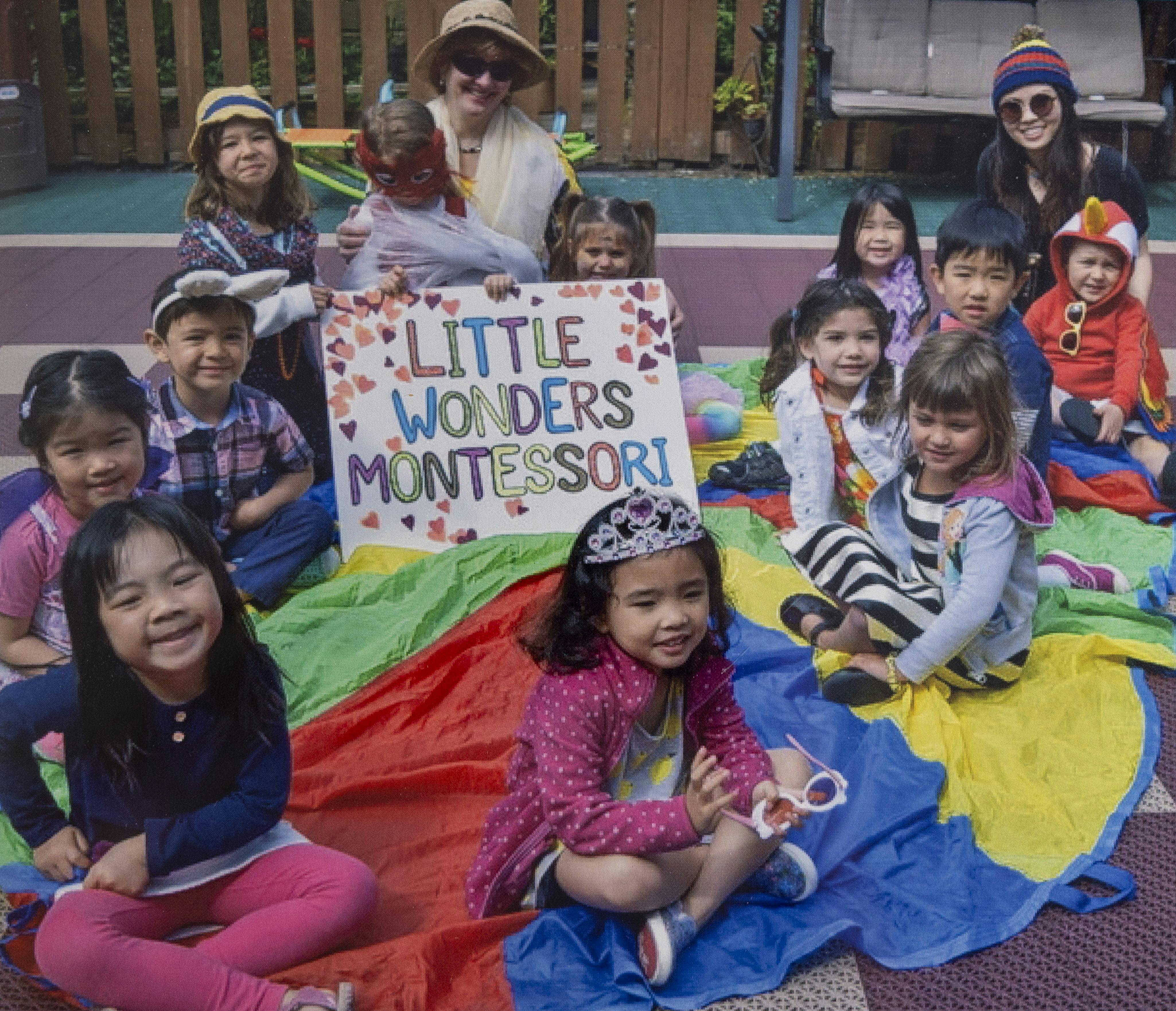 Group of children and adults holding a sign that reads "Little Wonders Montessori"