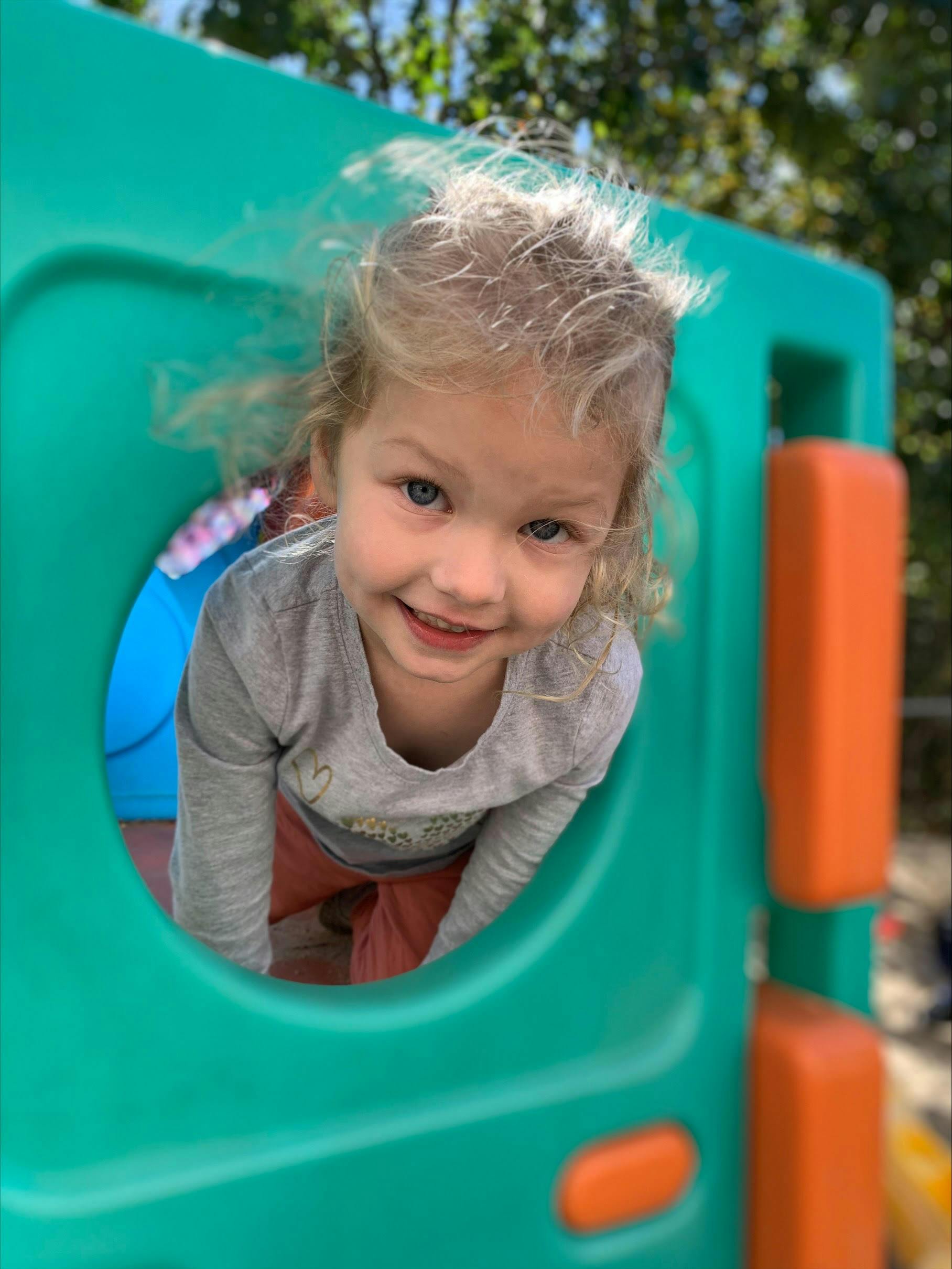 Child looking out from a round opening in a green plastic play structure