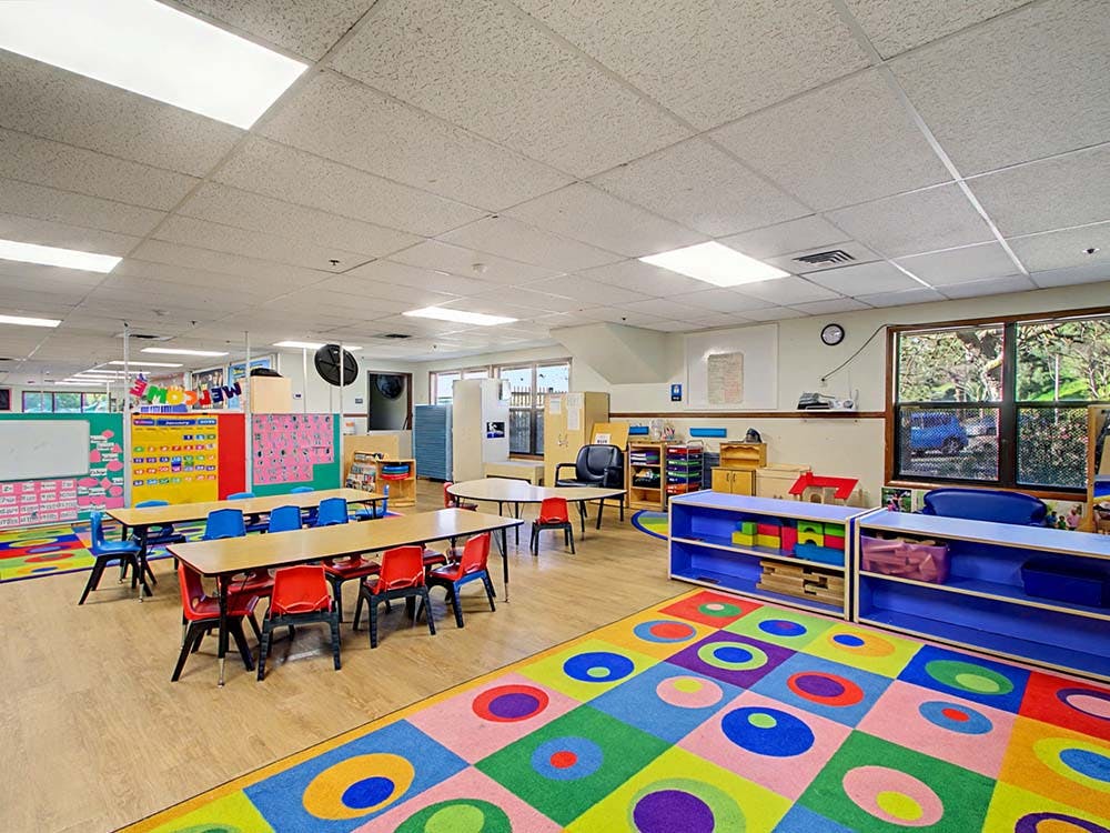 Classroom with small tables and chairs, colorful rug, and bulletin boards