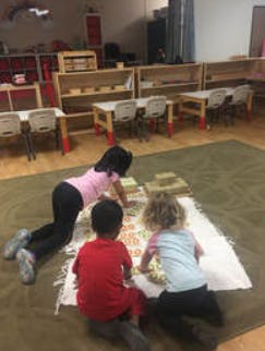Three children playing with blocks on a rug in a classroom