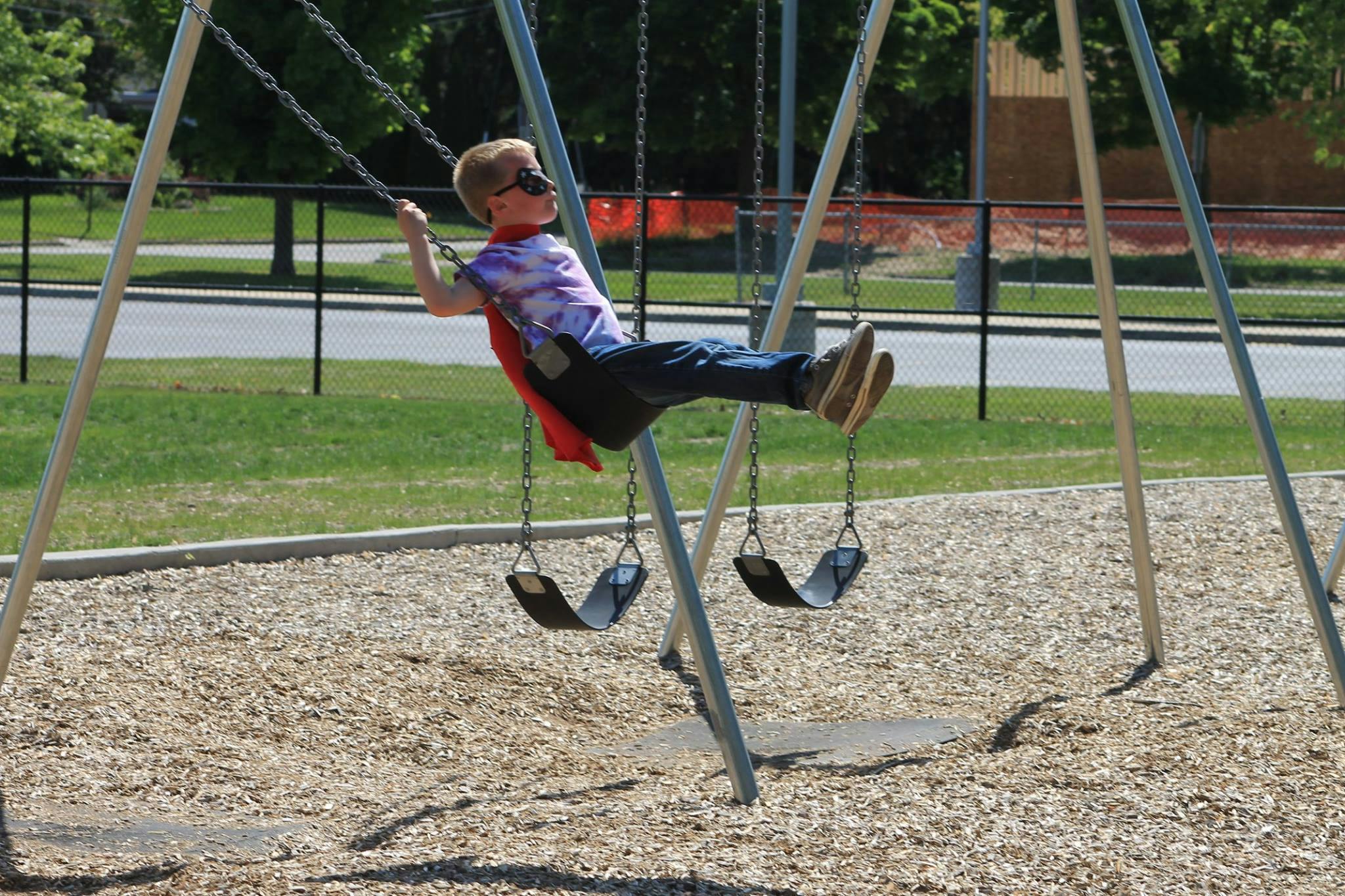 Child in a cape and sunglasses swinging on a playground