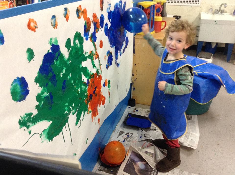 Child in an art smock painting on a large sheet of paper