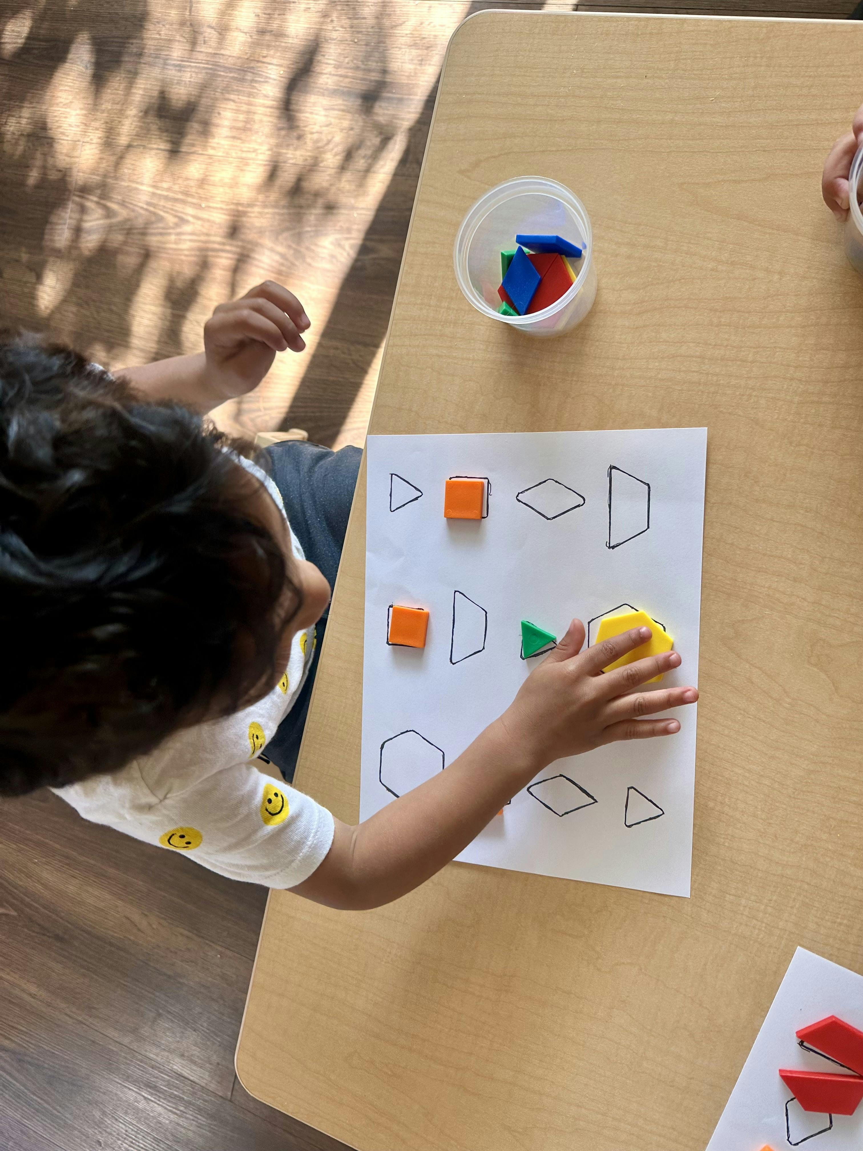 Child matching colored shape blocks to outlines on paper at table