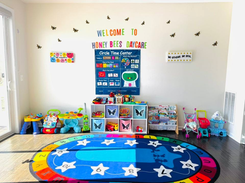Colorful playroom with a large rug, toys, and signs on the wall including "WELCOME TO HONEY BEES DAYCARE"