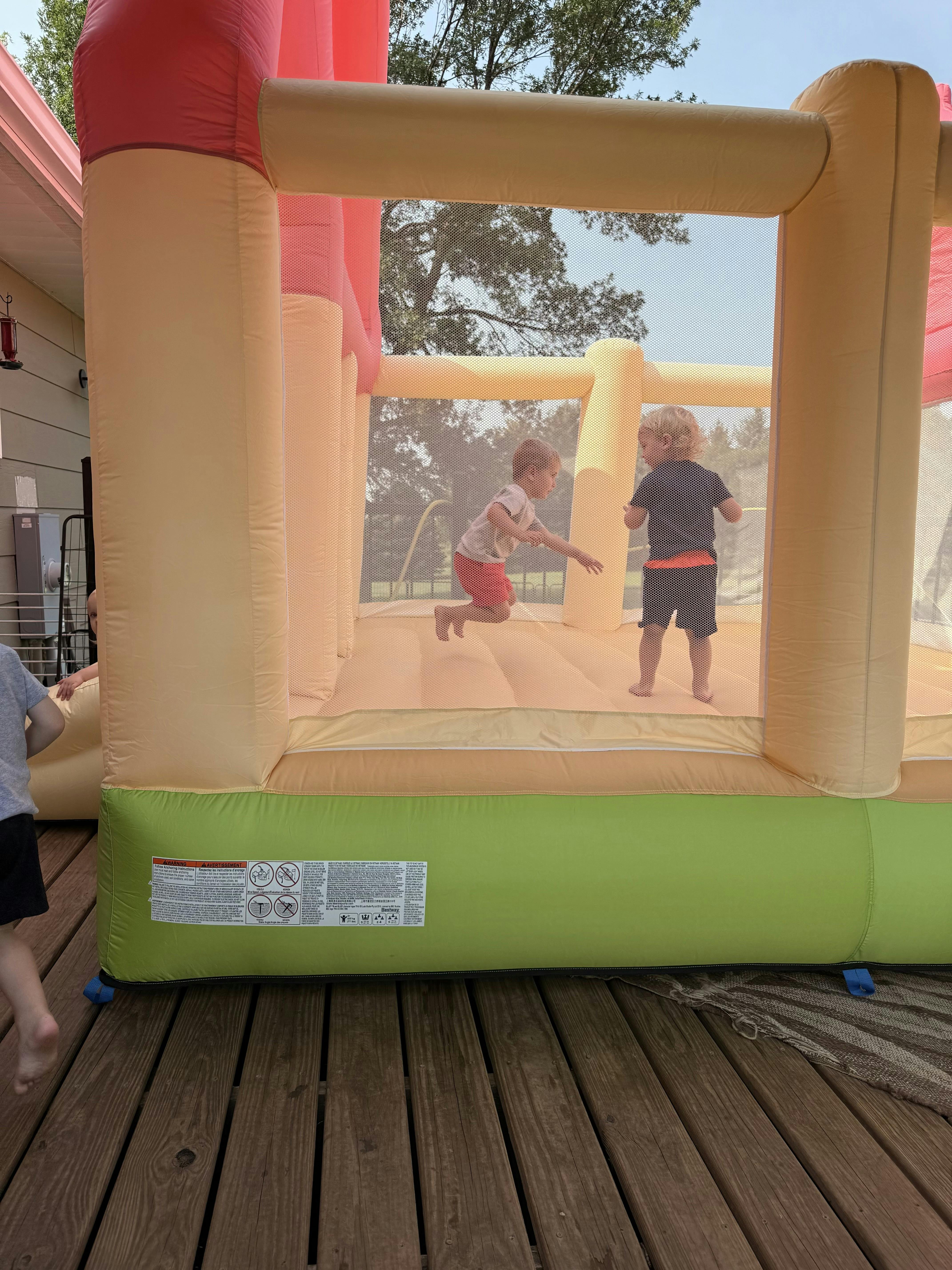 Two children jumping inside a bounce house on a wooden deck