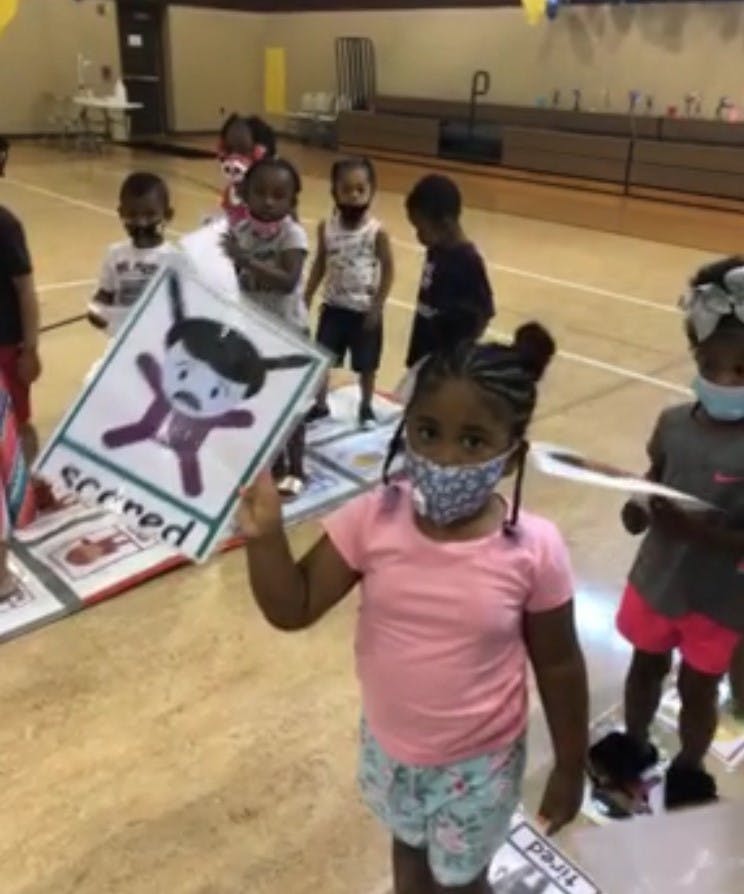 Child in a mask holding up a sign with a cartoon character and the word "scared"