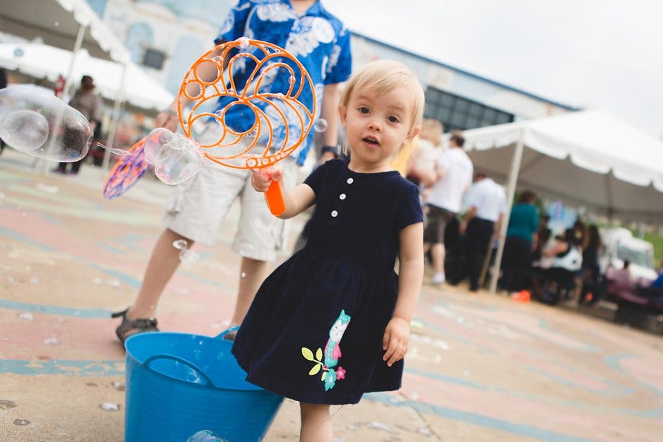 Child holding a bubble wand next to a blue bucket