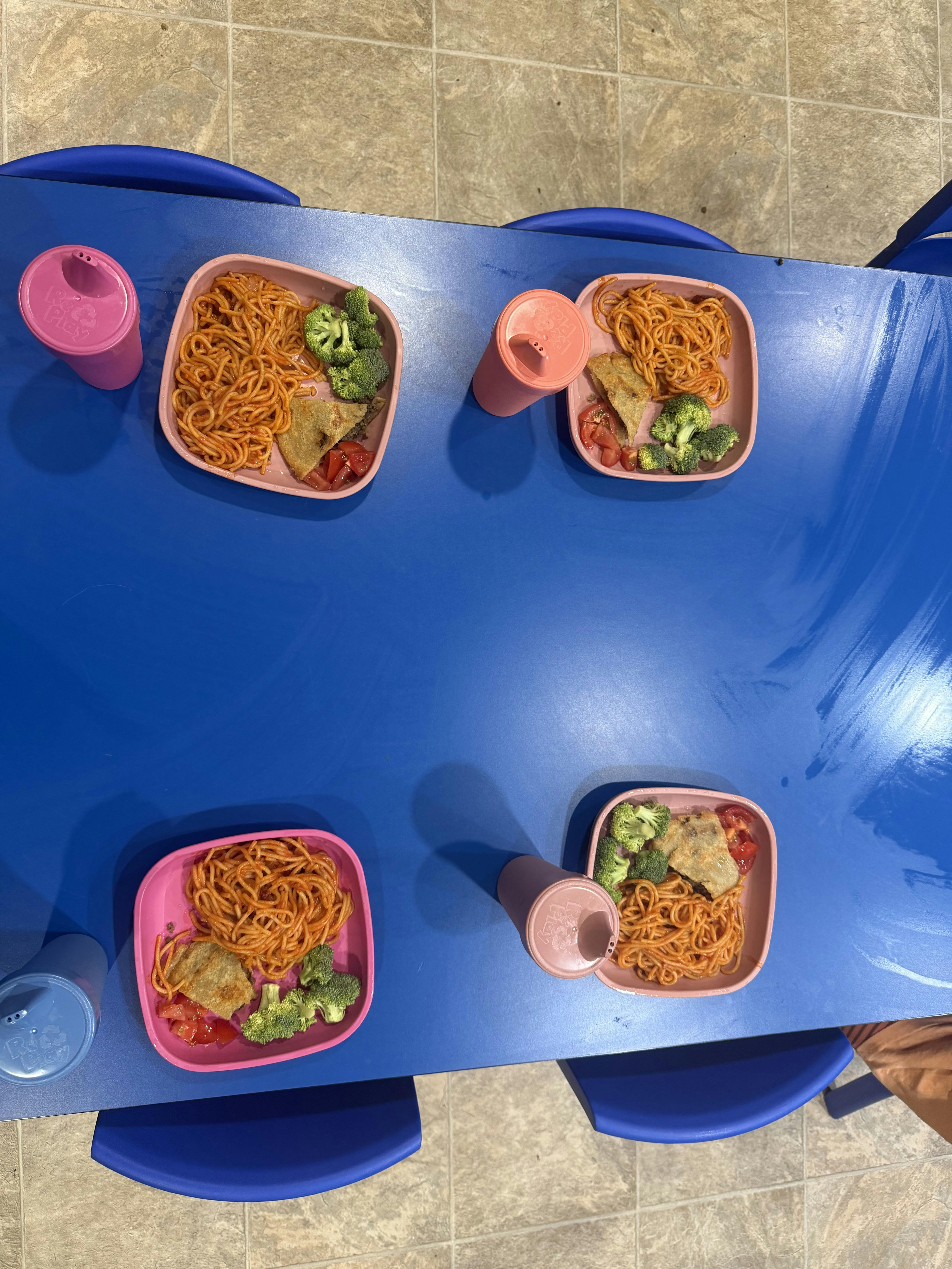 Four plates of spaghetti with broccoli and bread served on a blue table
