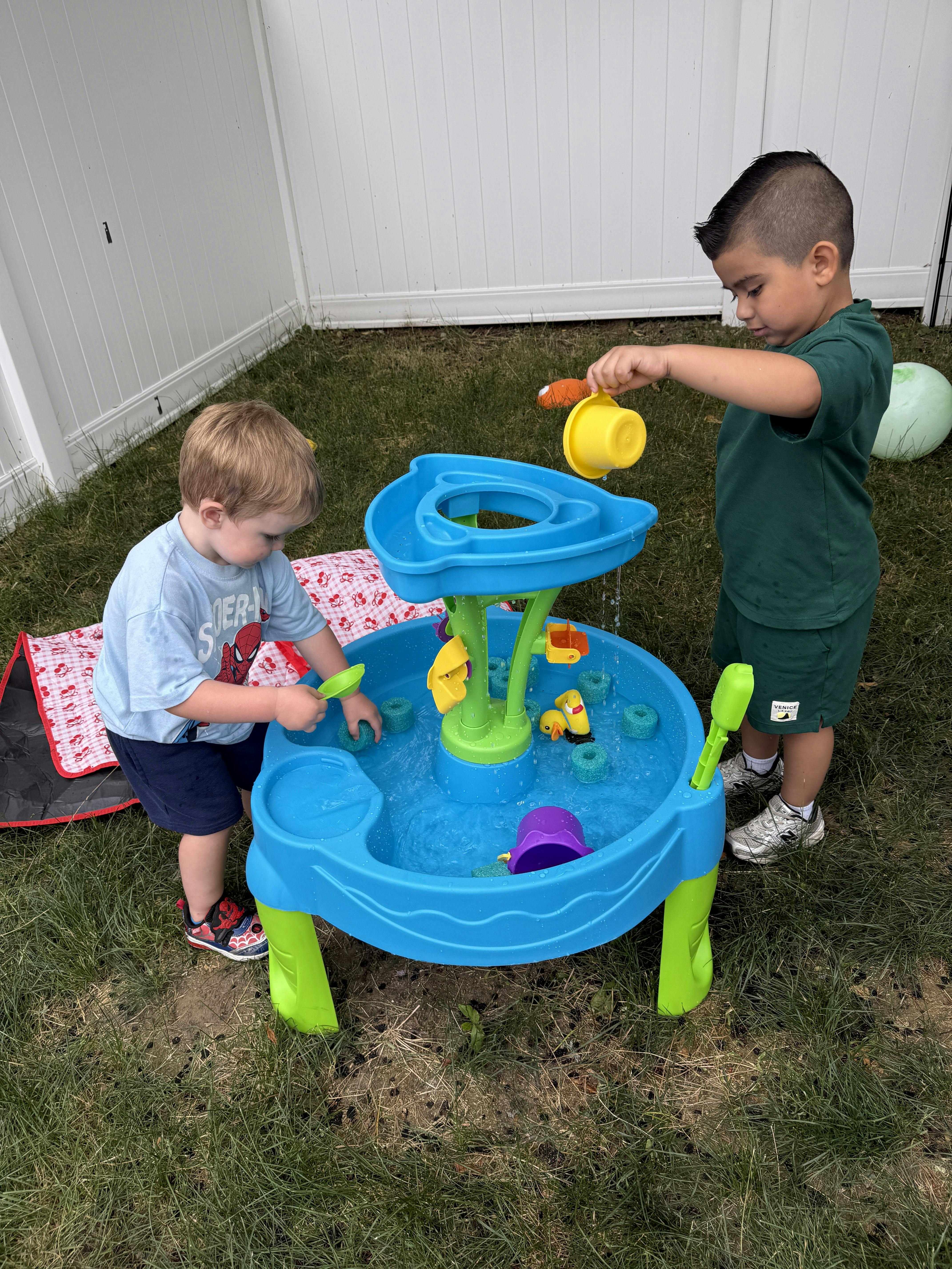 Two children playing with a plastic water table in a grassy yard