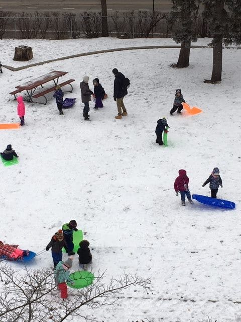 People and children playing in snow with sleds