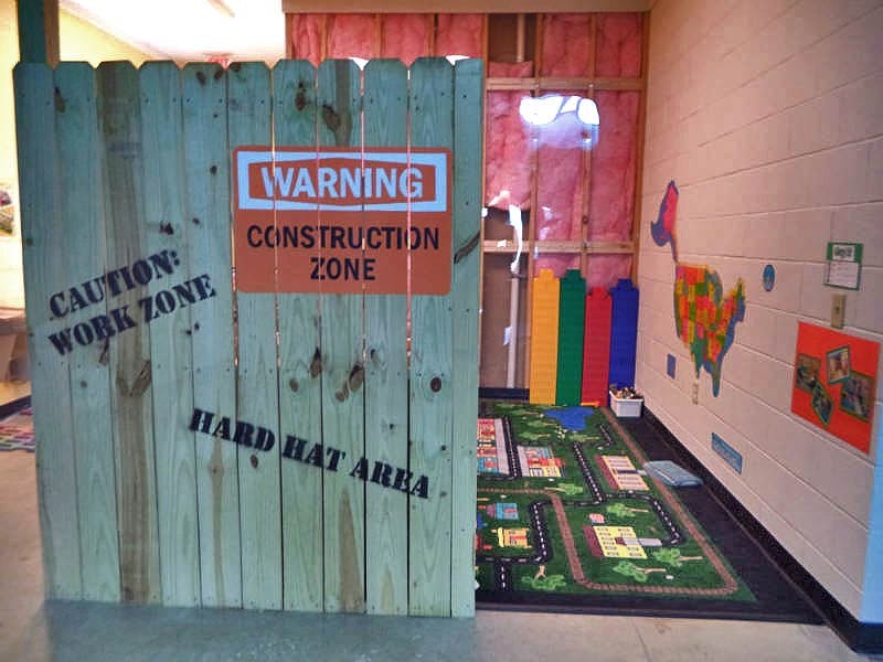 Wooden fence with "Warning Construction Zone" sign and play area