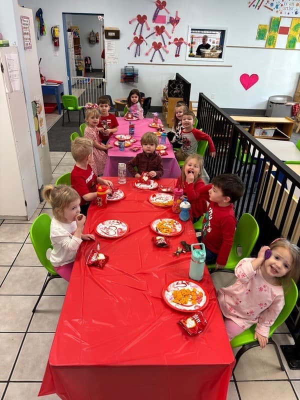Group of children seated at two tables with red tablecloths