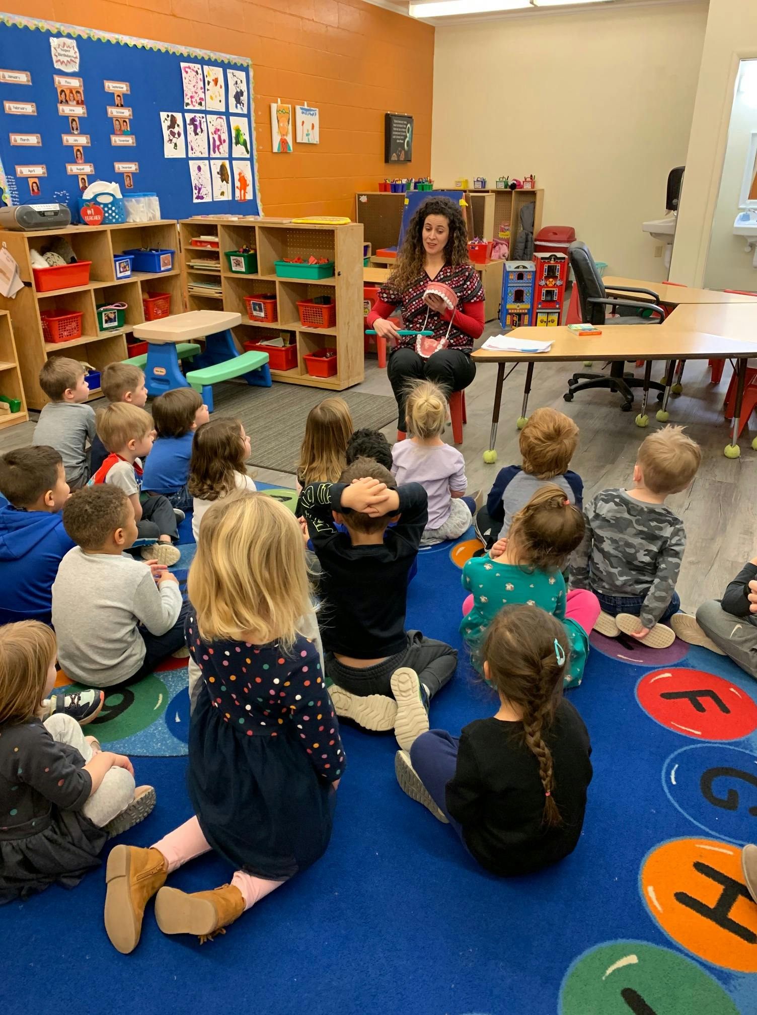 Adult showing a dental model to children sitting on a classroom floor