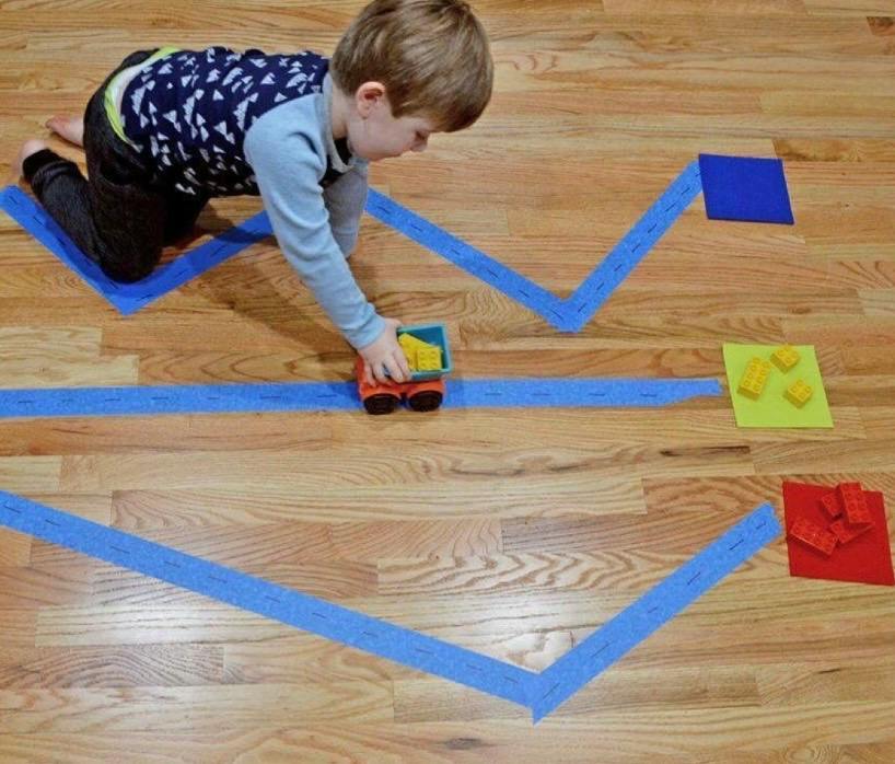 Child playing with a toy dump truck on paths marked by tape on a floor