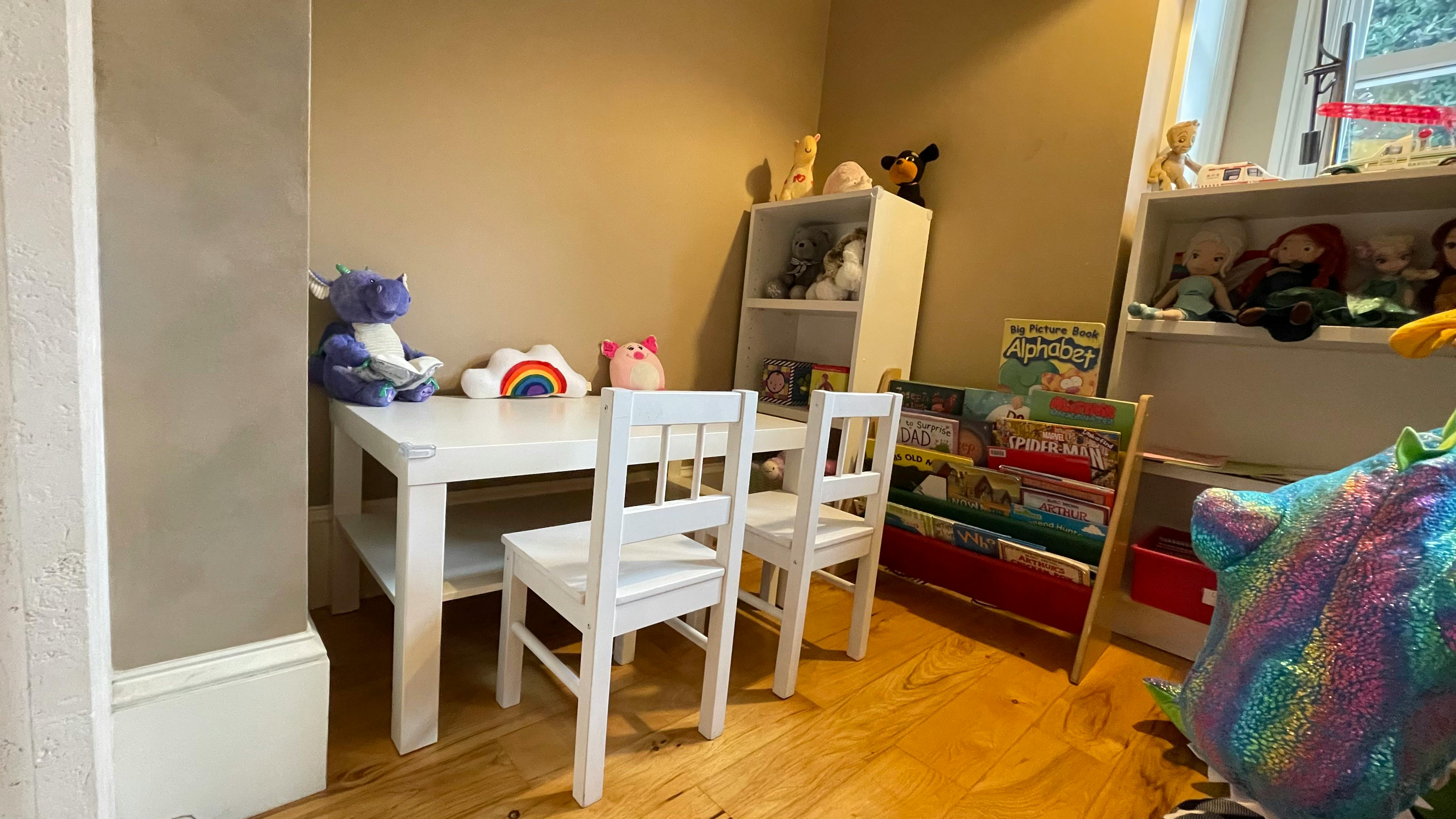 Children's play area with a white table, two chairs, and shelves with toys