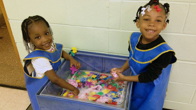 Two children playing with colorful objects in a water table