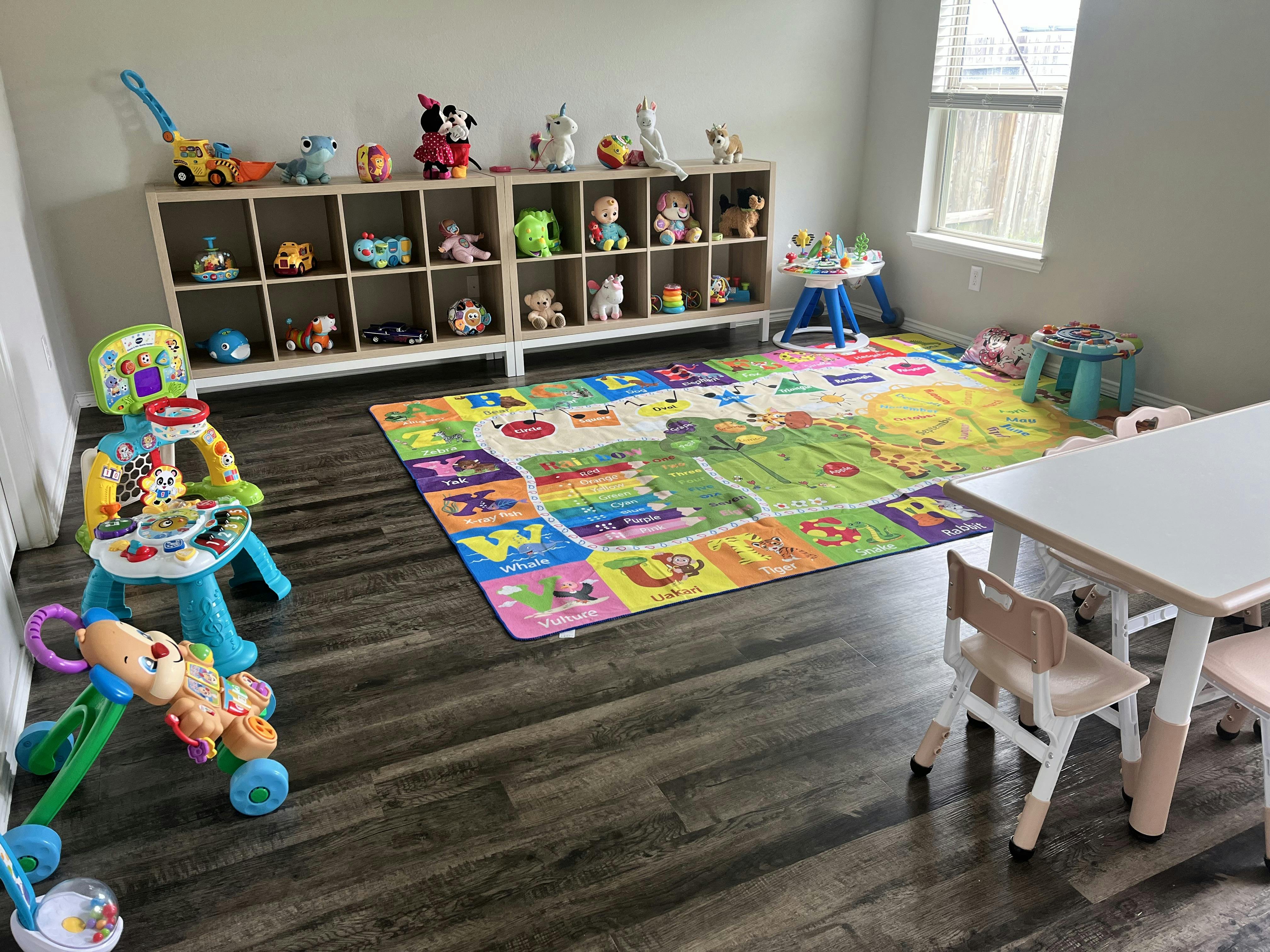 Playroom with toys on shelves, a colorful alphabet mat, and a small table and chairs