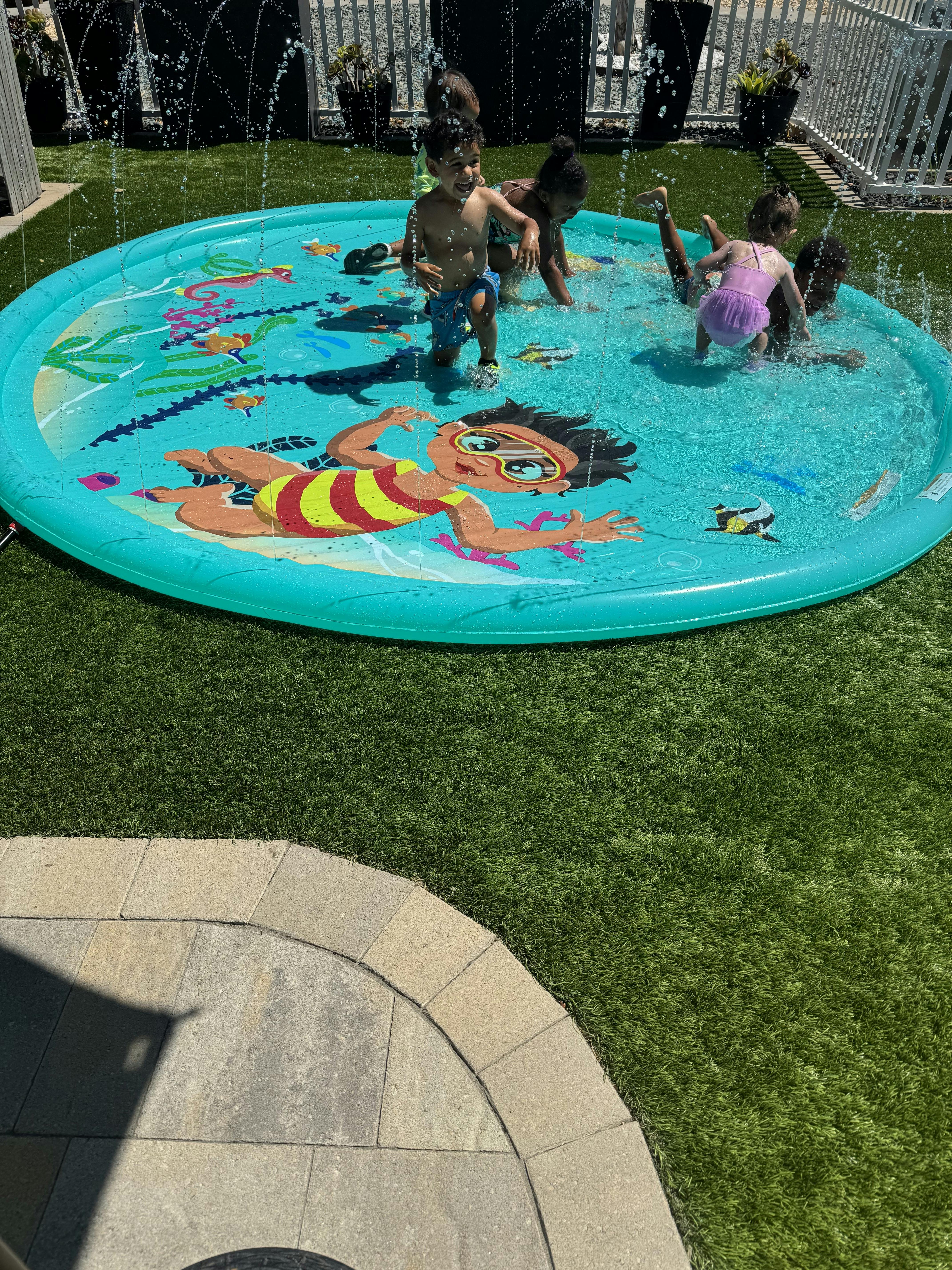 Children playing in a round water splash pad on grass