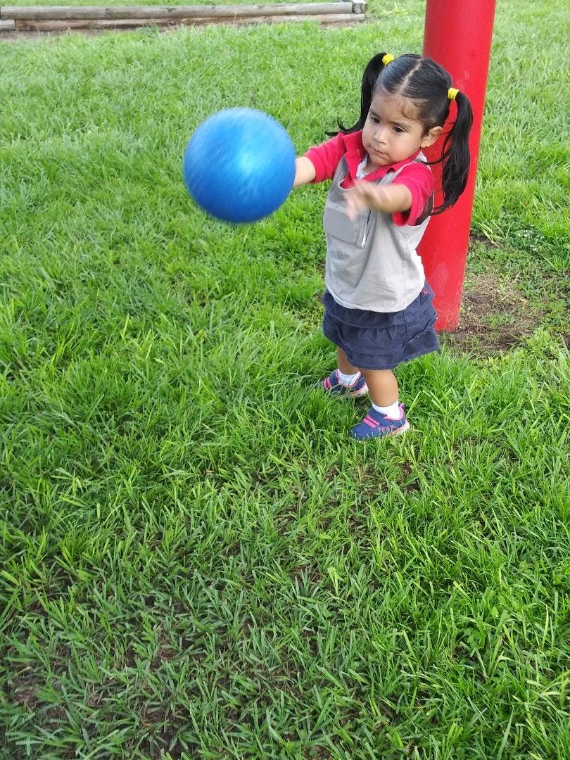 Child in pigtails holding a blue ball on a grassy lawn