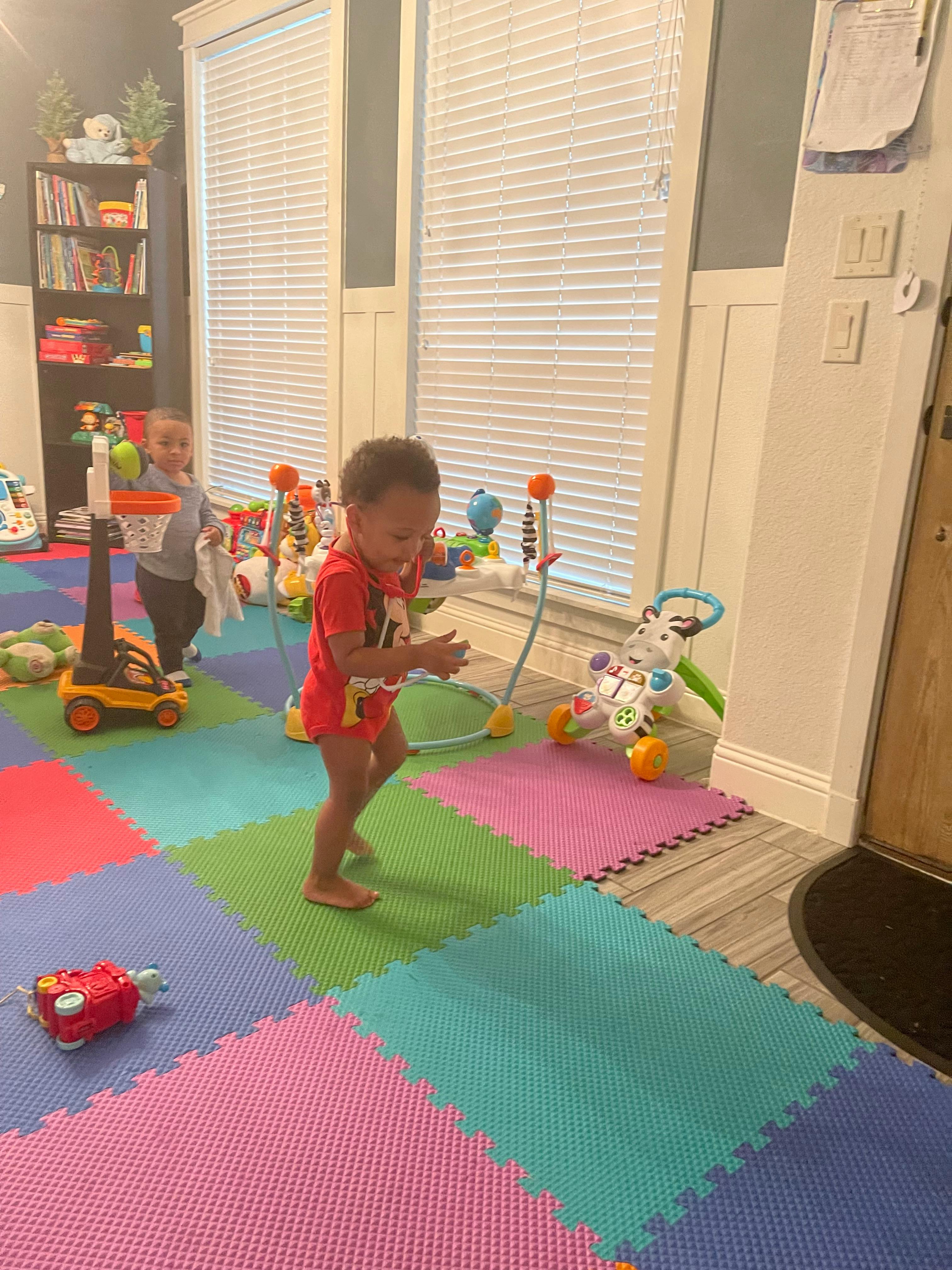 Two children playing on a colorful foam mat with toys