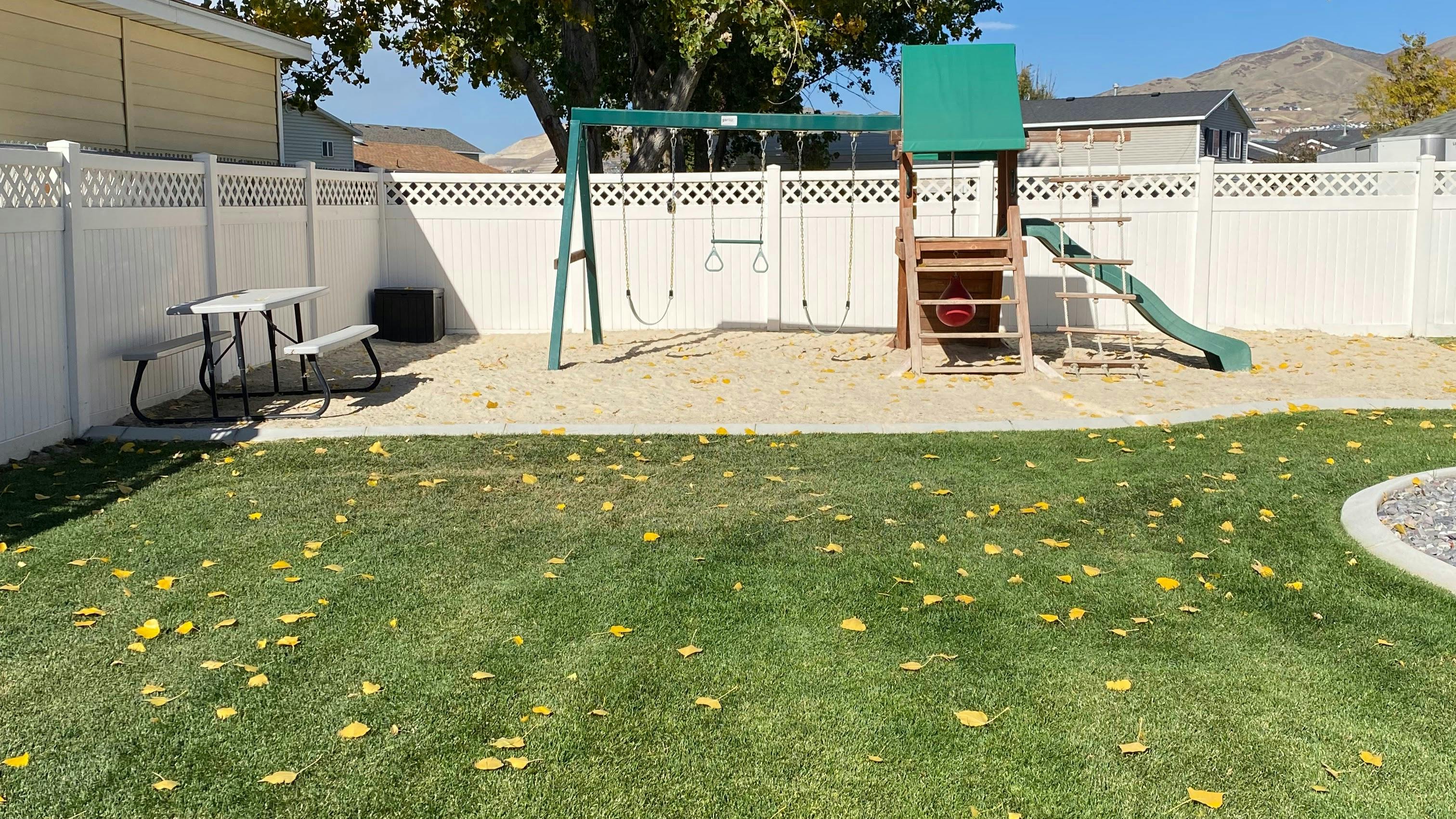 Backyard with a green lawn, white fence, picnic table, and playground set