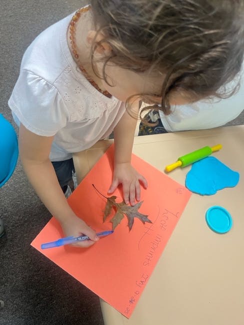 Child tracing a leaf on orange paper with a blue marker