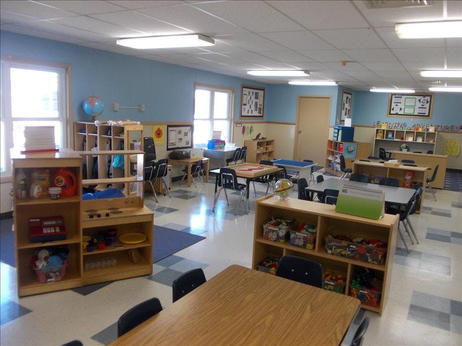 An empty early childhood classroom with small tables and chairs