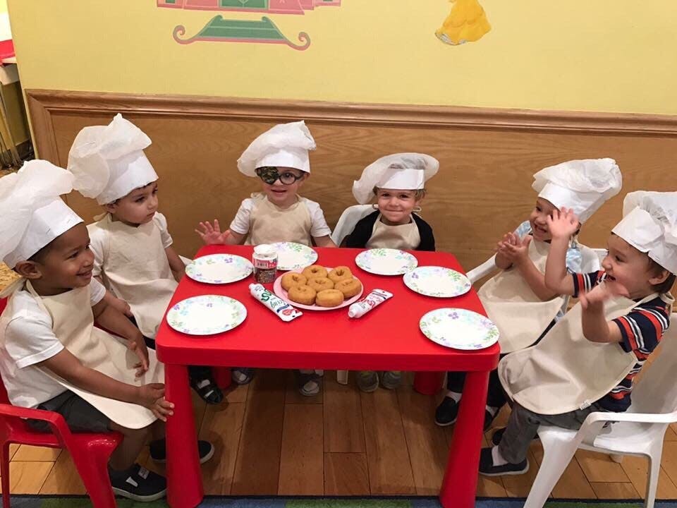 Children in chef hats and aprons sitting around a table with pastries
