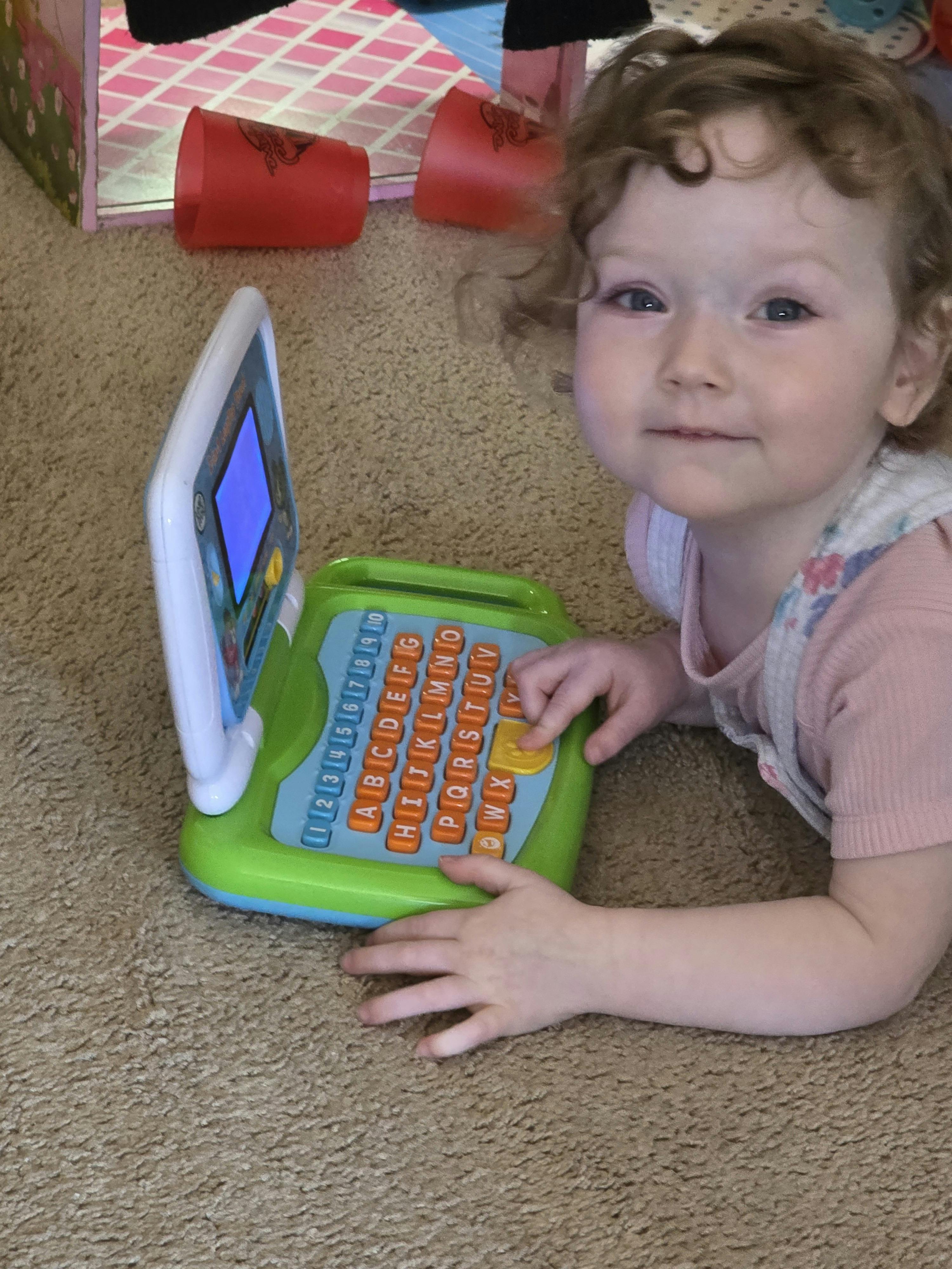 Child lying on the floor playing with a toy alphabet laptop