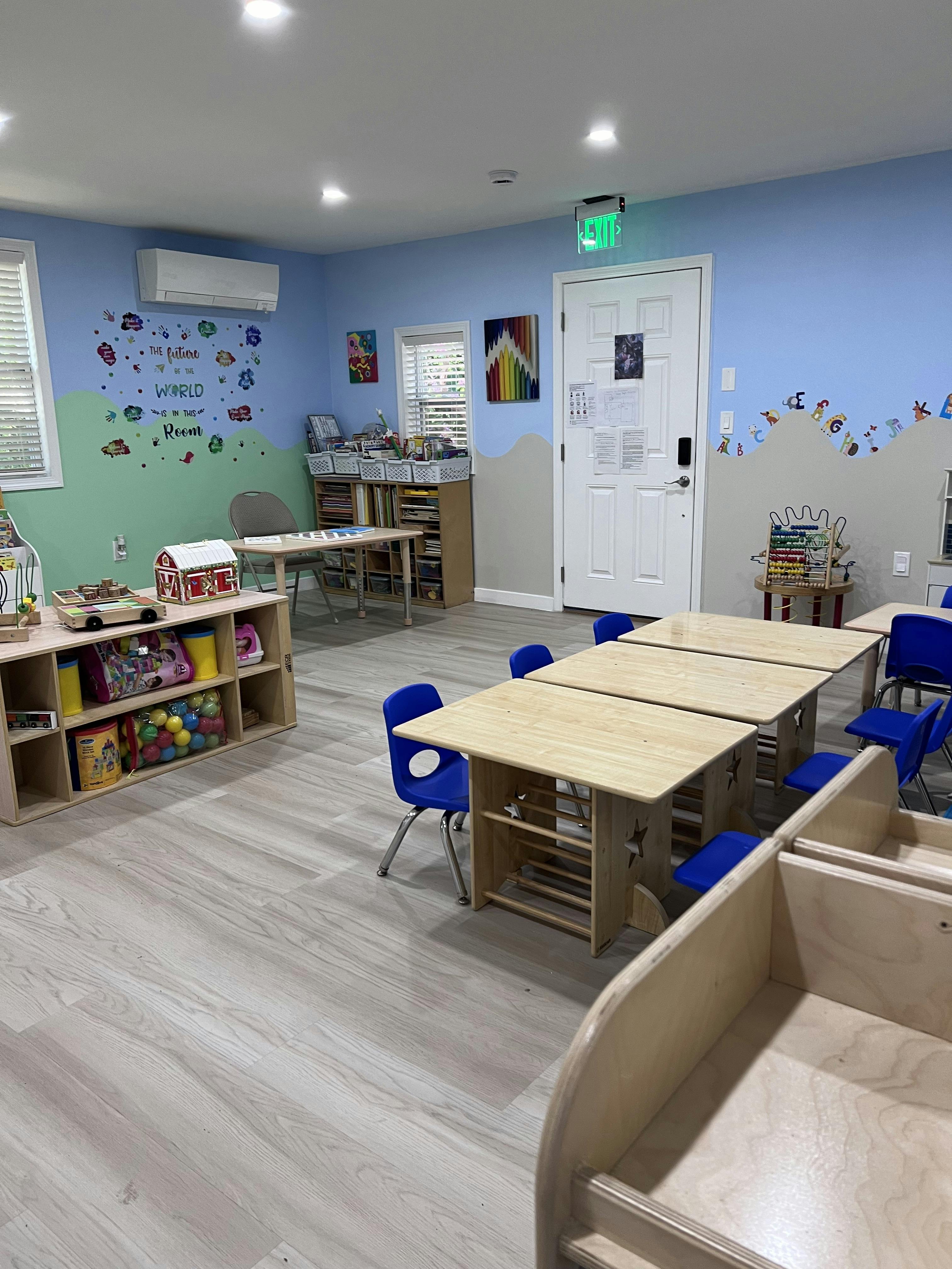 Children's classroom with wooden tables, blue chairs, and toy storage shelves