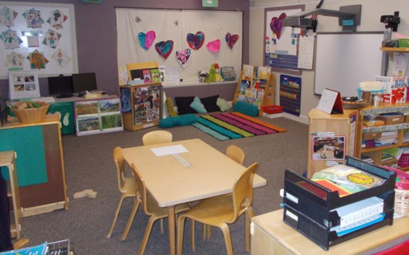 Empty classroom with small tables and chairs, shelves, and a colorful rug