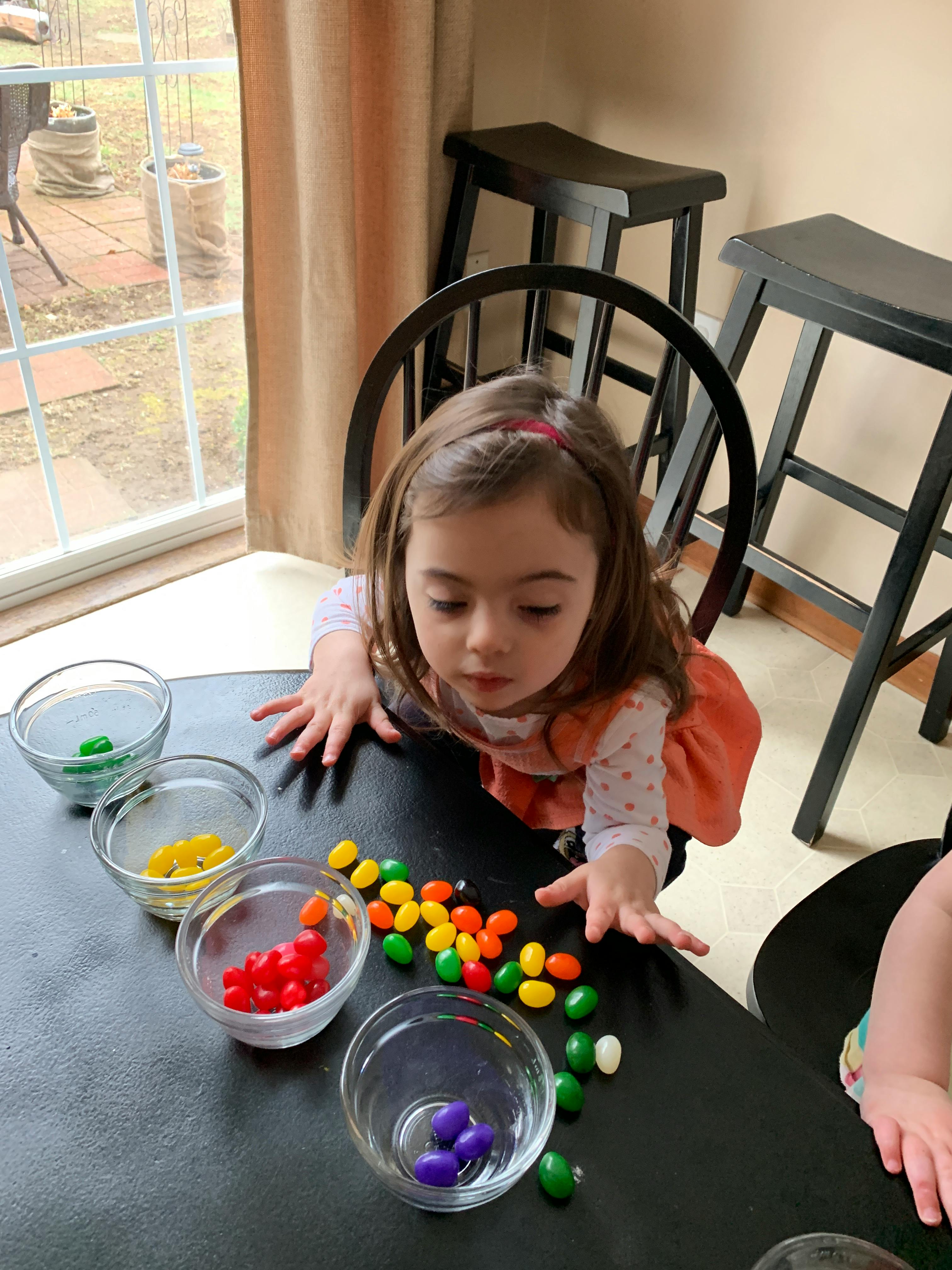 Child sorting colorful candies into small bowls on a table
