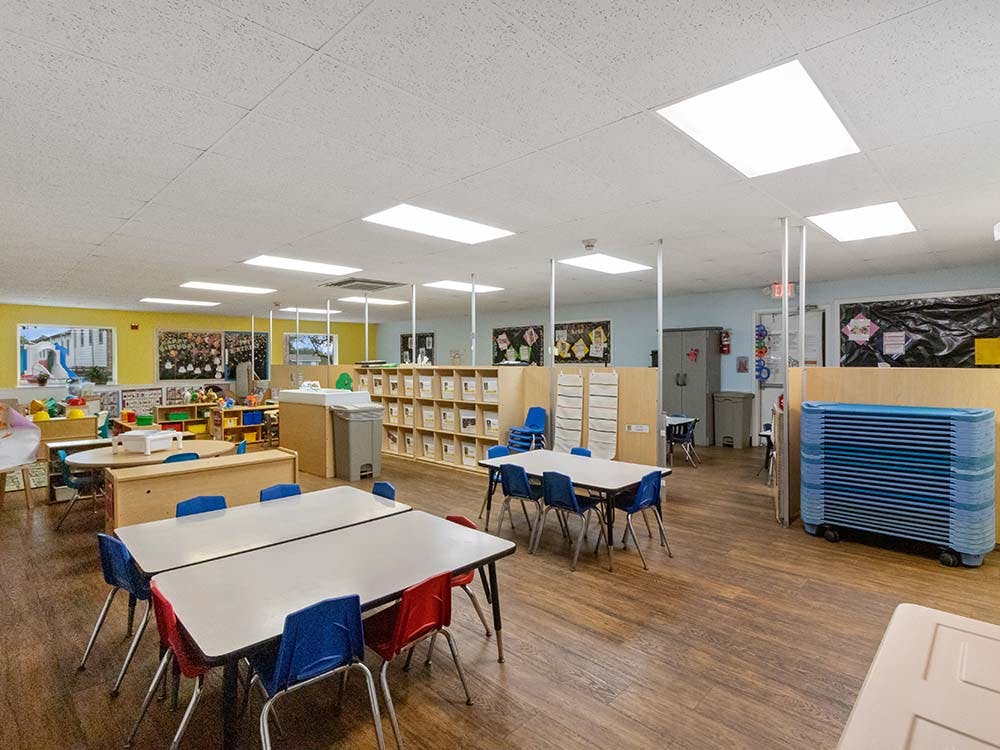 Empty classroom with small tables and chairs, shelves, and art on walls
