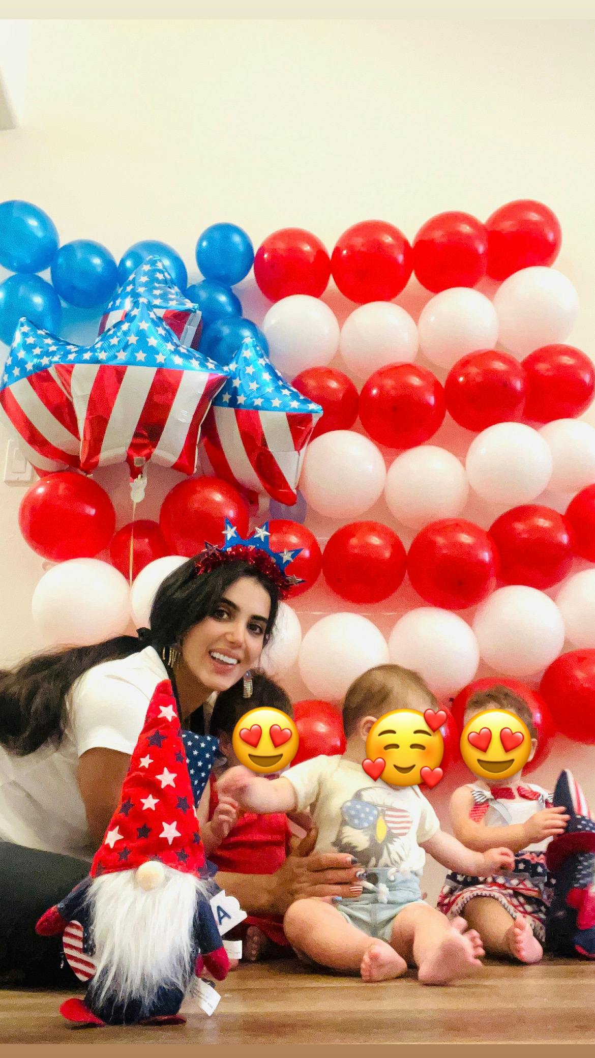 A person and three children posing with a patriotic gnome in front of balloons