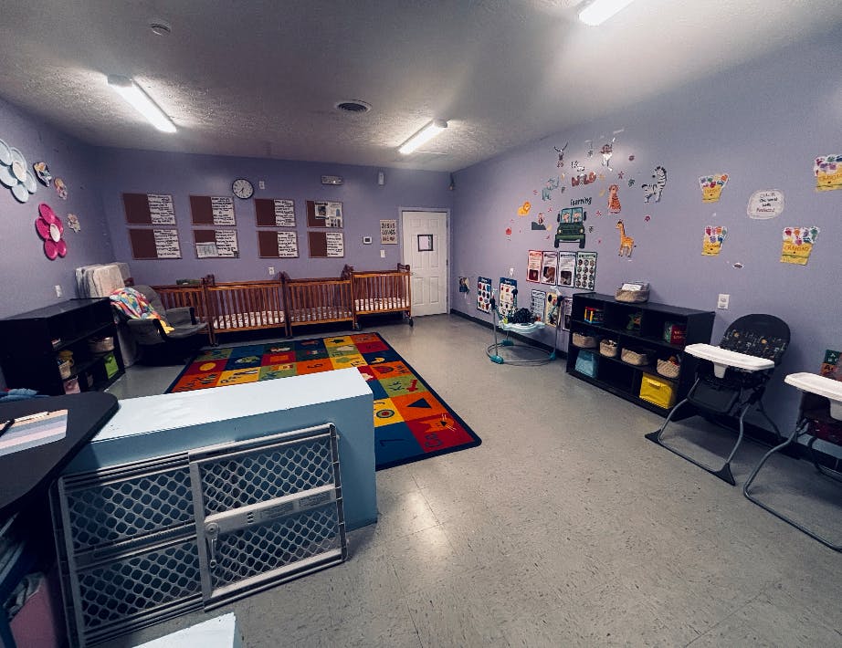 Childcare room with wooden cribs, floor rug, and high chairs
