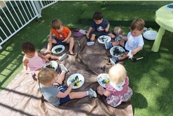 Group of children sitting on a mat outdoors painting with sponges
