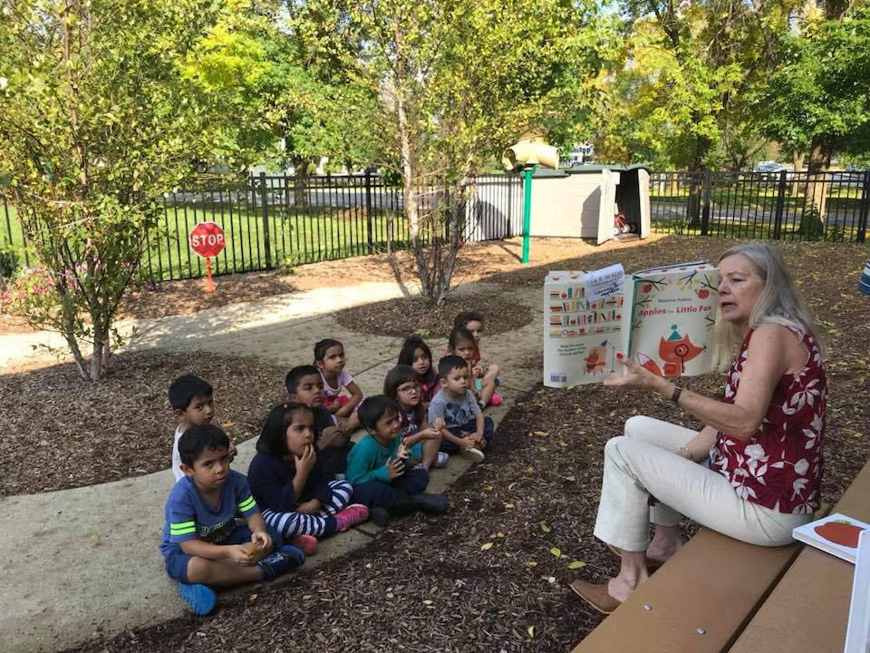 Person reading a book to a group of children outdoors