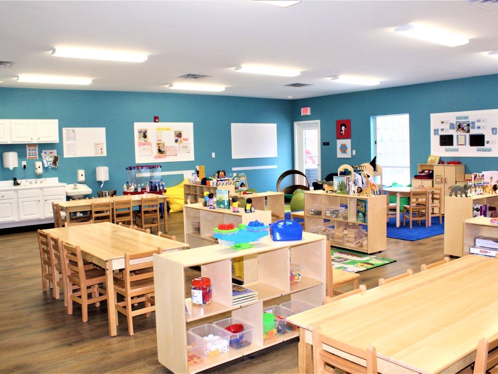 Classroom with child-sized tables and chairs, shelves with toys, and a sink