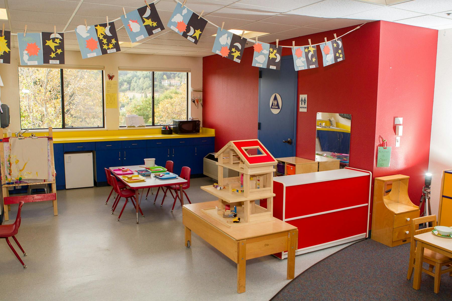 A colorful classroom with small tables and chairs, and artwork strung across the ceiling