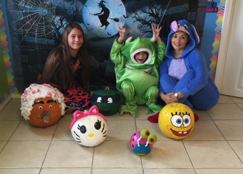 Three people in costumes with decorated pumpkins