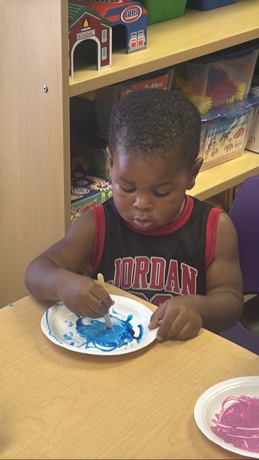 Child painting on a paper plate with a stick