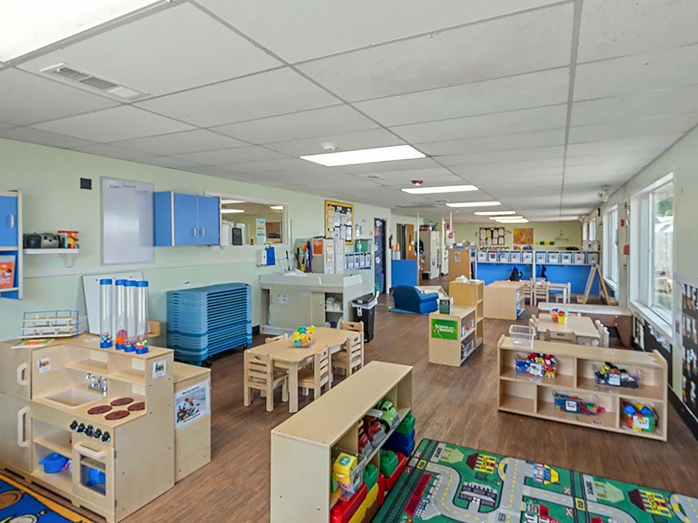 Empty classroom with small tables and chairs, play kitchen, and colorful rugs