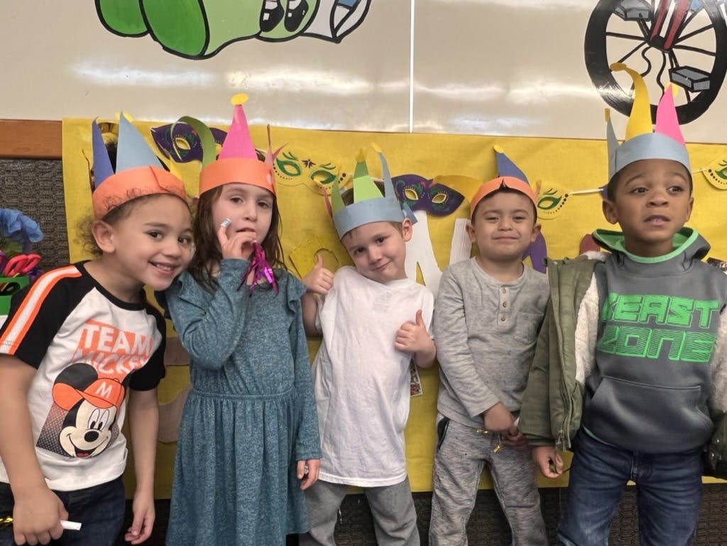 Five children wearing handmade paper hats in a classroom setting